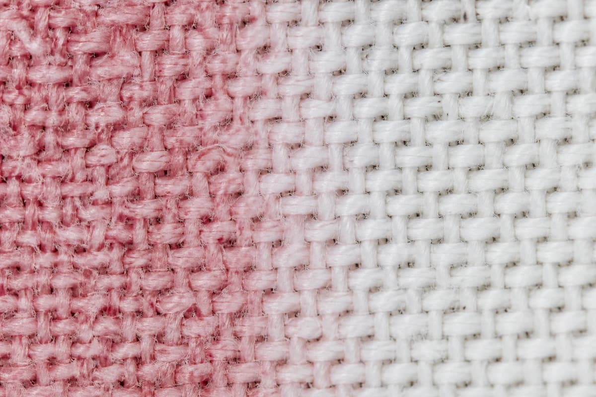 Macro canvas weave showing pink colour transfer beside cleaner fibres during sneaker stain removal Dubai assessment