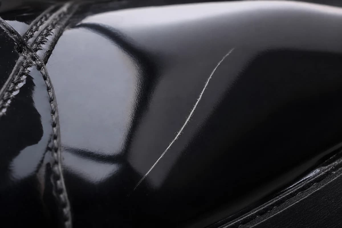 Macro close-up of patent leather gloss showing a light scuff line beside a restored mirror finish after premium material care Dubai